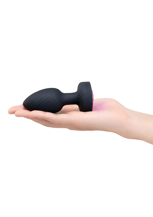 A black silicone butt plug with a textured ribbed shaft and a flared base, shown resting on an open hand against a plain white background.