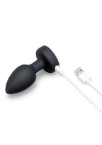 Black silicone butt plug with a textured grip, connected to a white USB charging cable, shown on a solid white background.